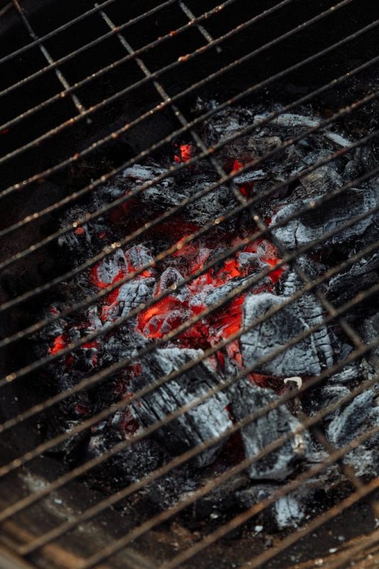 Detailed view of a charcoal grill with glowing red embers and ash, perfect for barbecue enthusiasts.